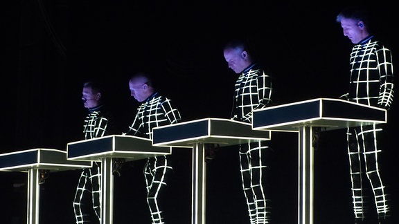 Die Mitglieder der Elektro-Band Kraftwerk stehen bei einem Auftritt an ihren Mischpulten.