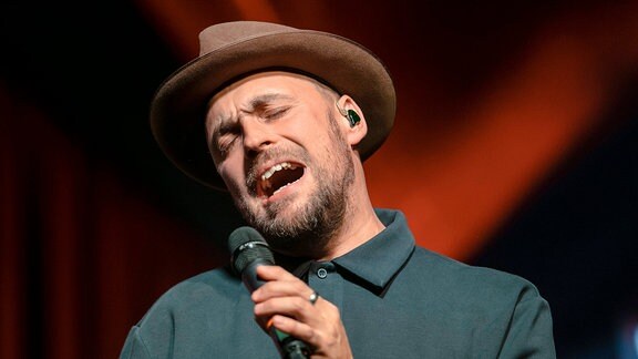 Sänger Max Mutzke trägt einen Hut und singt mit geschlossenen Augen auf einer Bühne