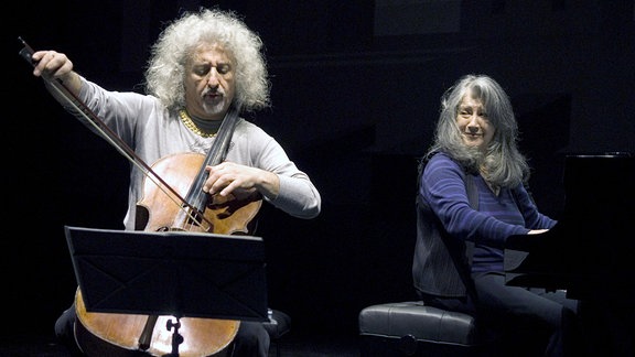 Ein Mann spielt Cello, eine Frau am Klavier sitzt lächelnd daneben