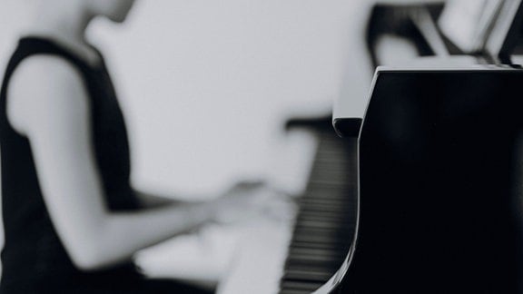 Eine Person sitzt an einem Konzertflügel und spielt Klavier.