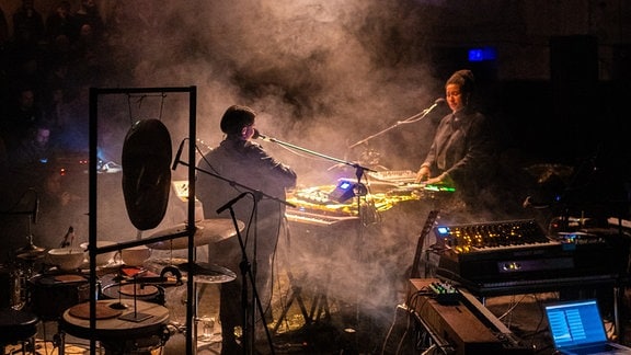 Die beiden Musikerinnen des Duos Olicia stehen sich bei einem Konzert auf der Bühne gegenüber. 