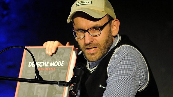 Sascha Lange, ein Mann mit Brille und Basecap hält ein Buch in der hand, darauf steht "Depeche Mode"