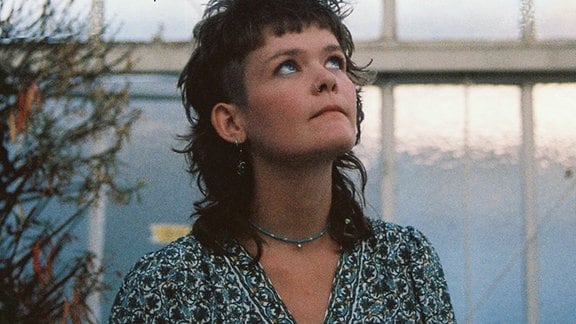 Die Singer-Songwriterin Sonny Casey mit braunharigem Vokuhila-Haarschnitt und im Kleid blickt nach oben in den Himmel.