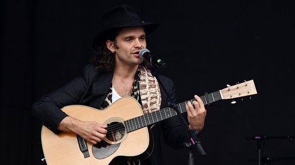 Tristan Brusch steht mit einer Gitarre an einem Mikrofon.