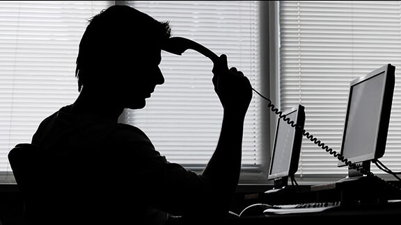 Ein Mann mit einem Telefonhörer in der Hand in nachdenklicher Pose vor einem Computer