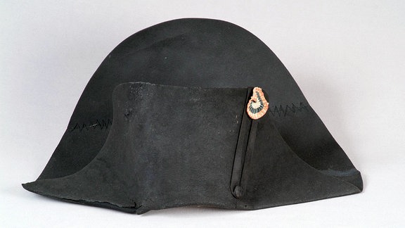 Ein historischer, schwarzer, halbrunder Hut vor einem neutralen Hintergrund.