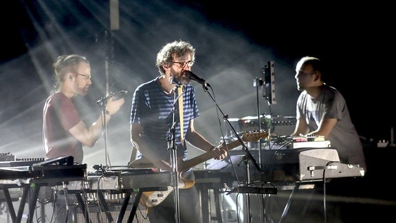 The Notwist auf der Bühne: drei Musiker mit Gitarre, Keyboard und Mikrofon