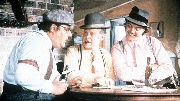 Filmszene - Drei Männer sitzen an einem Tisch und planen etwas.