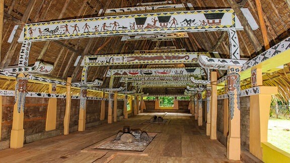 Historisches mikronesisches Versammlungshaus, am Boden Feuerstelle, darüber mit traditionelle Malerei von Jagdszene mit Krokodil verzierte Dachbalken von Palmendach