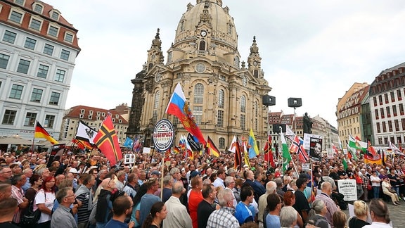 Viele Menschen auf einer Demonstration, dazwischen Fahnen wie eine zusammenmontierte deutsch-russische. Im Hintergrund die Frauenkirche.