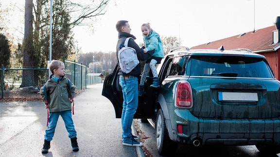 Vater und Kinder steigen aus einem Auto.