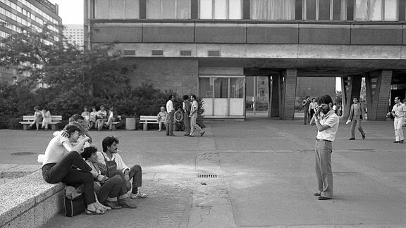 Schwarz-Weiß-Bild: Ein Mann fotografiert eine kleine Gruppe auf einem Platz.