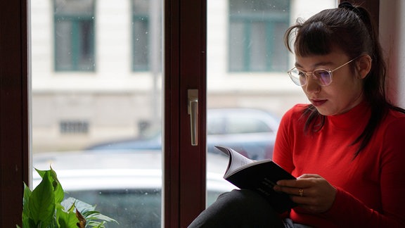 Die Autorin Ronya Othmann sitzt auf einer Fensterbank und liest.
