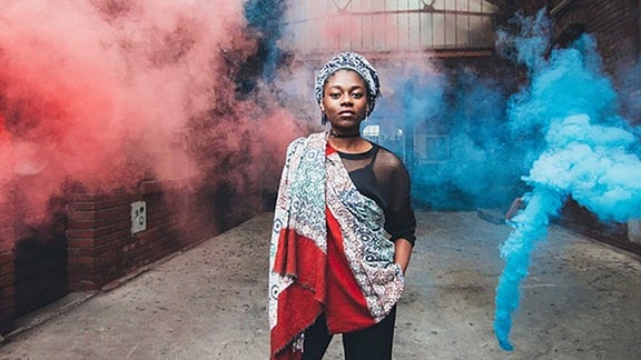 Die Musikerin Ki'Luanda ist umgeben von roten und blauen Rauchwolken 