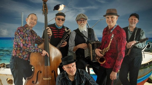 Die sechs Musiker der Band Jams posieren mit ihren Instrumenten vor einem Boot