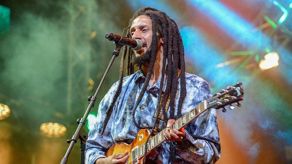 Musiker Julian Marley steht mit einer Gitarre auf einer Bühne und singt