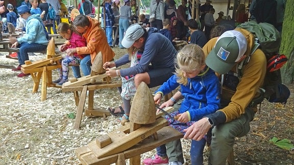 Familien sitzen an Geräten zur Holzbearbeitung