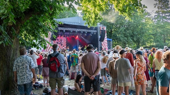 Publikum vor einer blau und rot beleuchteten Konzertbühne in einem Park beim Rudolstadt-Festival