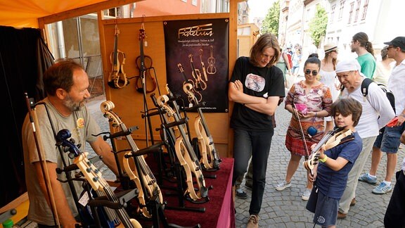 Mehrere Menschen stehen vor einem Stand in Rudolstadt, wo mehrere Gitarren auf einem Tisch stehen.