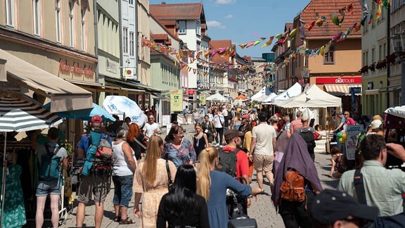 Viele sommerlich gekleidete Menschen sind unterwegs in einer mit Wimpeln geschmückten Fußgängerzone einer Kleinstadt