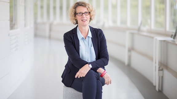 Sabine Wolfram, Direktorin am smac – eine Frau mit blonden Locken, einer dunklen Brille, sie trägt ein helles Hemd und dunkle Hose und ein Sakko