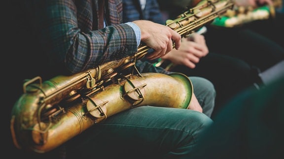 Ein Saxophonist hat sein Saxophon auf seinem Schoß liegen.