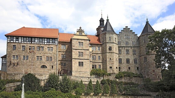 Blick auf eine leicht erhöht stehende Schlossanlage mit Springbrunnen und einem Park