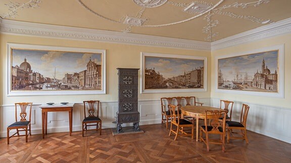 Ein Raum in Schloss Wörlitz, mit Holzparkett, Bildern an den Wänden, einem Tisch und mehreren Stühlen.