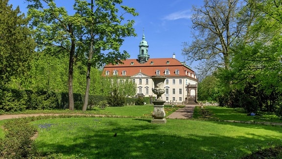 Ein Barockgarten mit einer Skulptur, im Hintergrund ist das  Schloss Lichtenwalde zu sehen.