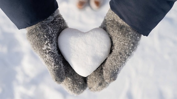 Ein Herz aus Schnee liegt in zwei Händen mit Handschuhen.