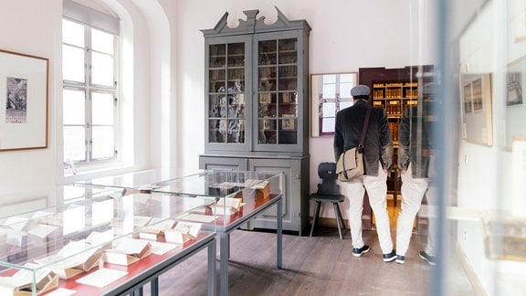 Ein historischer Raum mit Ausstellungstischen voller Bücher, eine Person schaut in einen Glaskasten.