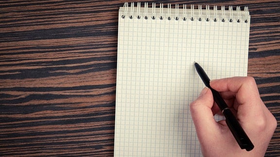 eine Hand mit Kugelschreiber setzt zum Schreiben im Schreibblock an
