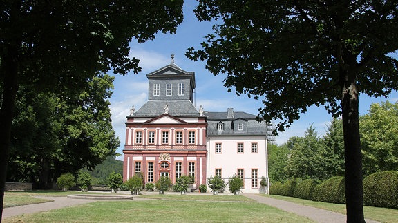 Schwarzburg Kaisersaalgebäude, Blick über eine Wiese auf ein rötliches Gebäude mit dunklem Dach. 