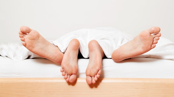 Zwei Paar Füße hängen aus einem Bett.
