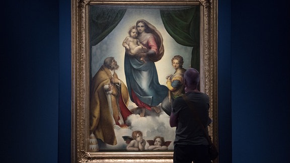 Ein Mann steht in einer Ausstellung vor dem Ölgemälde Die Sixtinische Madonna von Anton Hille