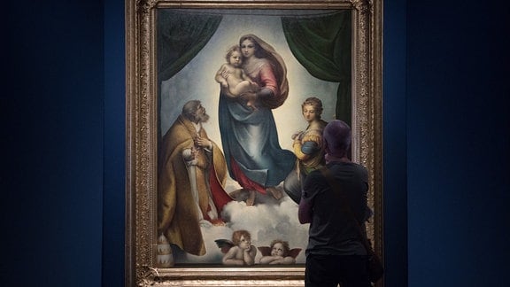 Ein Mann steht in einer Ausstellung vor dem Ölgemälde Die Sixtinische Madonna von Raffael