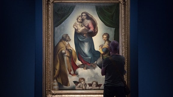 Ein Mann steht in einer Ausstellung vor dem Ölgemälde Die Sixtinische Madonna