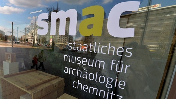 Das Logo für das Staatliche Museum für Archäologie Chemnitz (SMAC) ist an einem Schaufenster des Gebäudes in Chemnitz zu sehen. 