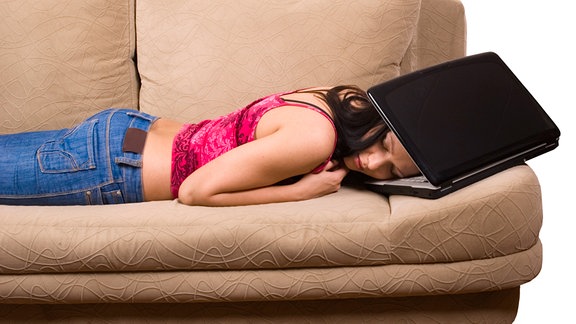 Frau liegt auf Sofa, ihren Kopf zwischen Monitor und Tastatur eines Notebooks gesteckt