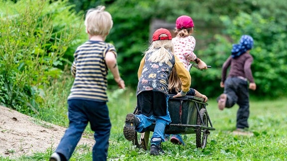 Kinder einer Kita spielen im Wald mit einem Anhänger