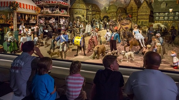 Fünf Personen sitzen im Deutschen Spielzeugmuseum vor Kirmesfiguren.