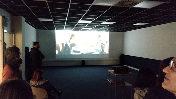 ein dunkler Raum mit Kinoleinwand, die Vereinsmitglieder probieren die Technik ihres neuen Studiokinos aus.