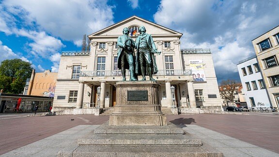 Ein Denkmal mit Goethe und Schiller stehend, dahinter ein großes Gebäude.