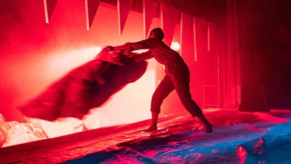 Auf einer Bühne steht eine Person in rotem Licht und schwenkt ein Tuch.