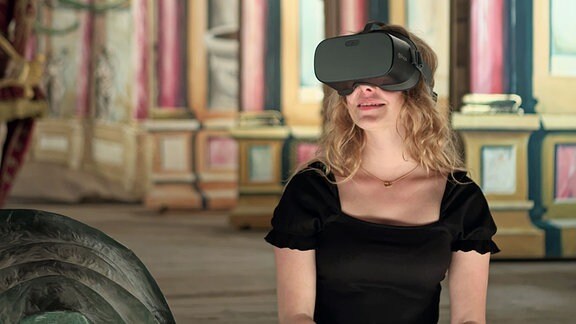 Besucherin trägt eine VR Brille auf dem Kopf und schaut sich im Sitzen um.