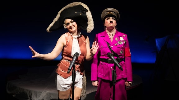Michaela Dazian trägt als Friedrich der Große einen breiten Hut, Antonia Marie Waßmund als Hitler eine rosa Uniform.