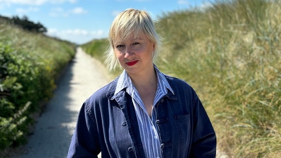 Eine Frau mit blonden Haaren auf einem Weg zwischen Dünen