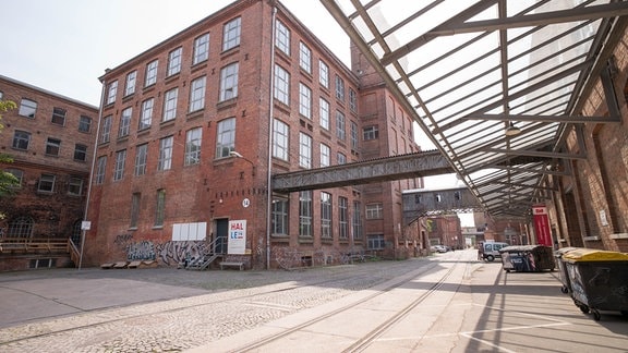 Blick auf ein ehemaliges Industriegelände mit roten Backsteingebäuden, Verbindungsgängen aus Stahl und Glas, Kopfsteinpflaster und Schienen
