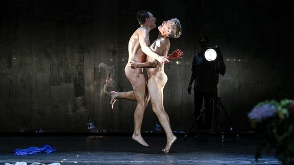 Zwei nackte Männer springen auf einer Bühne in die Höhe