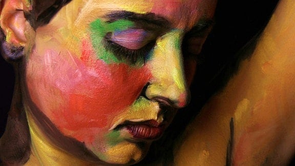 Der Kopf einer Frau ist von der Seite fotografiert, sie ist im expressionistischem Stil mit vielen Farben angemalt.